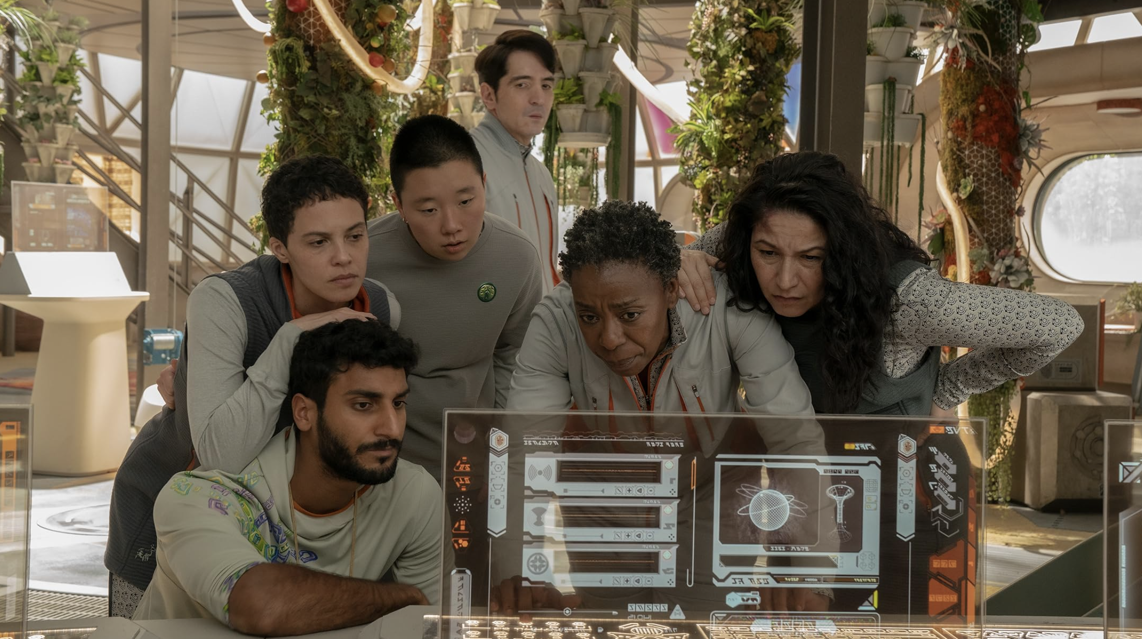 A group of six people stand around a computer screen.