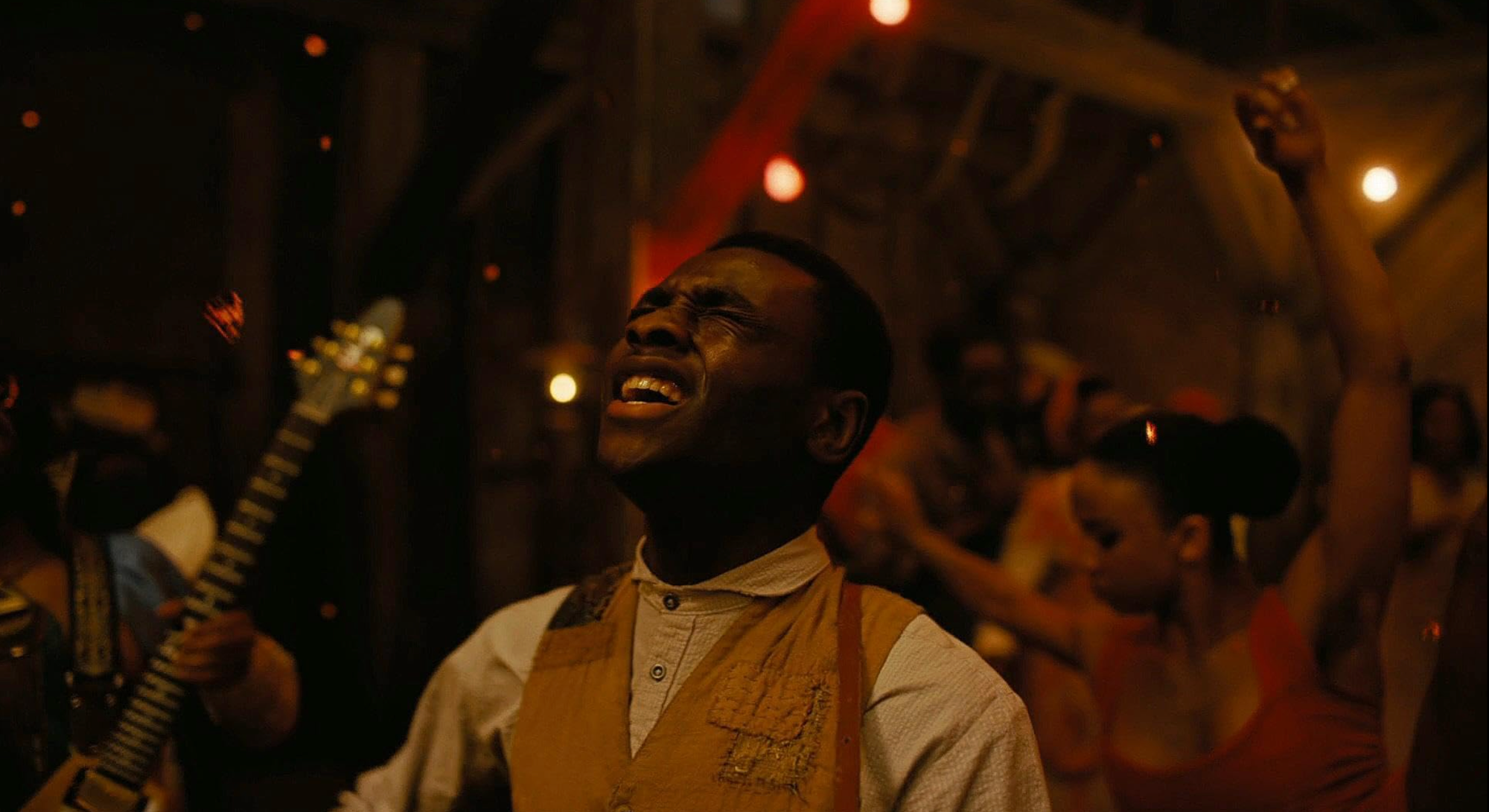 A young man in 1930s dress, sings with his whole heart while playing guitar. Behind him, the spirits of the past and future dance and bring their own music.